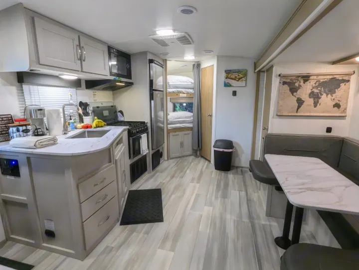 This RV rental interior features a modern kitchen, light wood-look flooring, dining booth, and bunk beds for comfortable travel.. Cruiser Rv Corp Other 2024