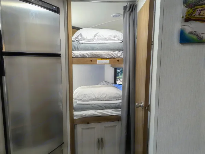 This RV rental interior features bunk beds with bedding, a stainless steel fridge, and a partial door, highlighting compact living.. Cruiser Rv Corp Other 2024