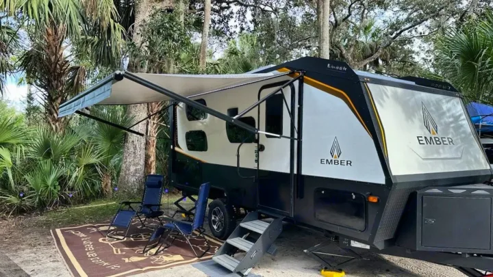 Ready for adventure! This Ember RV rental is perfectly set up at a palm-lined campsite with an extended awning and cozy seating.. Ember 191MBD 2022