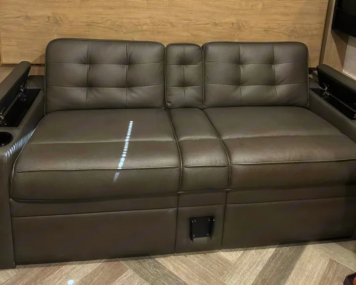 RV rental interior features: Dark gray tufted sofa with cup holders and armrest storage for travel comfort.. Ember 191MBD 2022