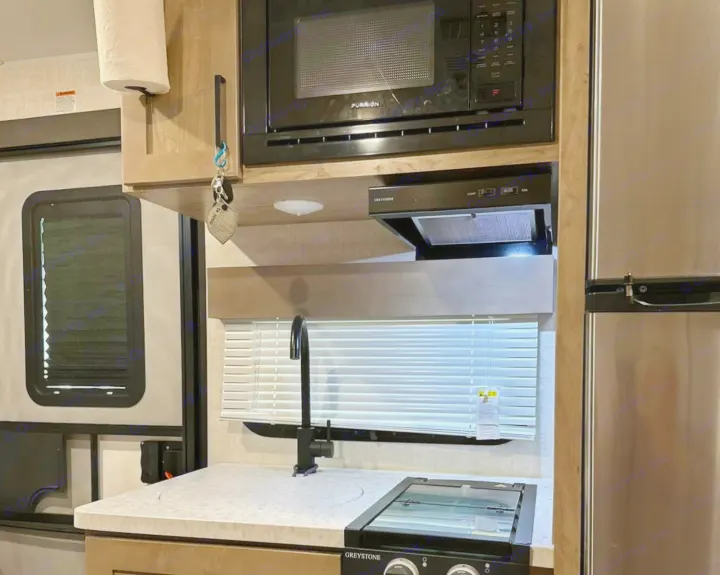 Clean, modern RV rental kitchen featuring a microwave, range hood, sink, and stovetop. Perfect for road trips.. Ember 191MBD 2022