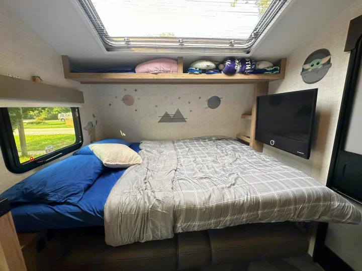 Cozy RV rental bedroom with a large bed, overhead skylight, mounted TV, and fun Grogu decor. Includes window views.. Ember 191MBD 2022