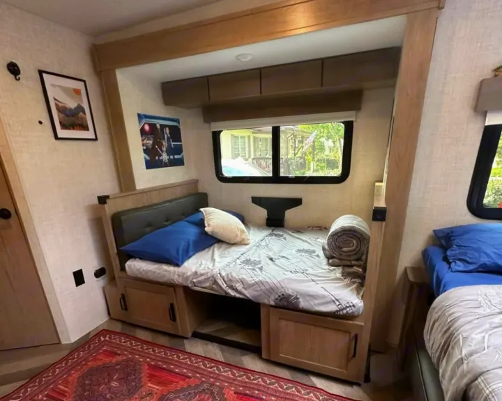 RV rental interior: two beds with blue pillows, built-in storage, and windows offering views. A perfect travel setup.. Ember 191MBD 2022