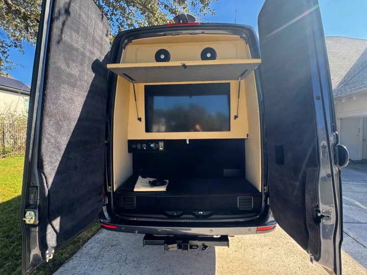RV rental: Rear view of a custom camper van with open doors, revealing a TV, speakers, and bed inside. Ready for adventure!. Midwest Automotive Designs Ultimate Presidential 2020