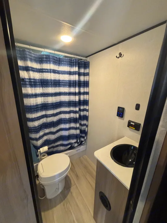 Explore this well-appointed RV rental bathroom featuring a toilet, blue striped shower, and sleek vanity with a black sink.. Coleman Coleman 23 B 2025