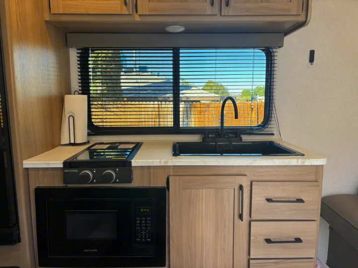 Modern RV rental kitchen with black sink, stove, microwave, and light wood cabinets, offering home-like amenities on the road.. Coleman Coleman 23 B 2025