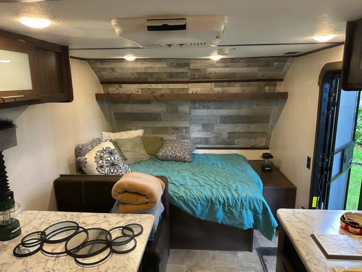 RV rental bedroom featuring a teal comforter, wooden headboard, and ample pillows, designed for compact travel comfort.. Coleman 17b 2022