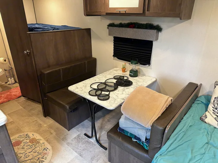 Cozy RV rental interior featuring a dining booth, bunk bed, and compact living space. Ideal for travel trailer adventures.. Coleman 17b 2022