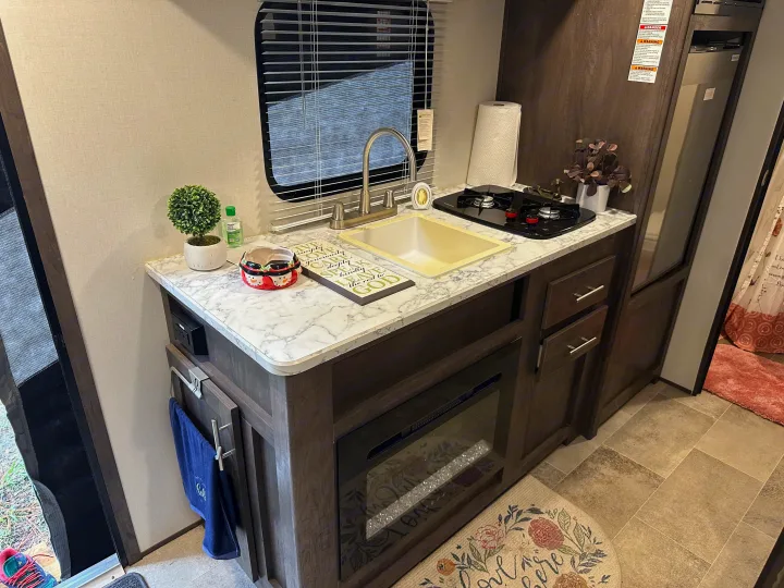 This RV rental offers a compact kitchen with a sink, stovetop, electric fireplace, and marble-look countertop.. Coleman 17b 2022
