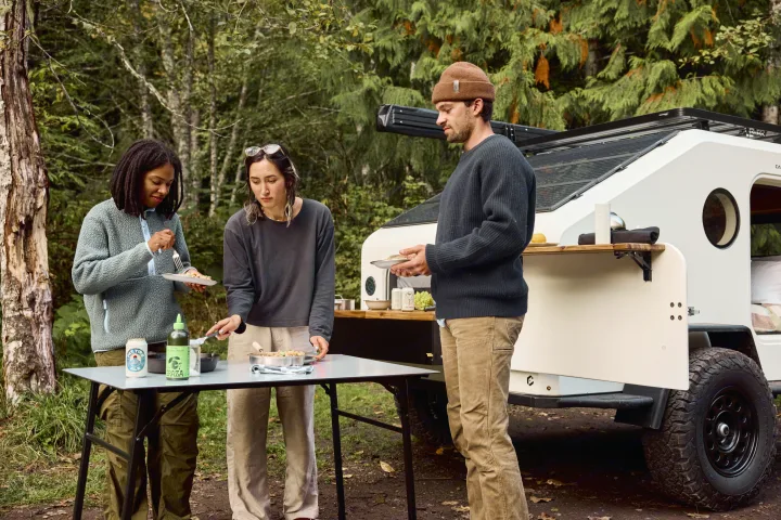 Friends enjoy outdoor cooking beside their modern RV rental travel trailer, perfect for camping adventures.. Campworks NS-1 Electrified 2024