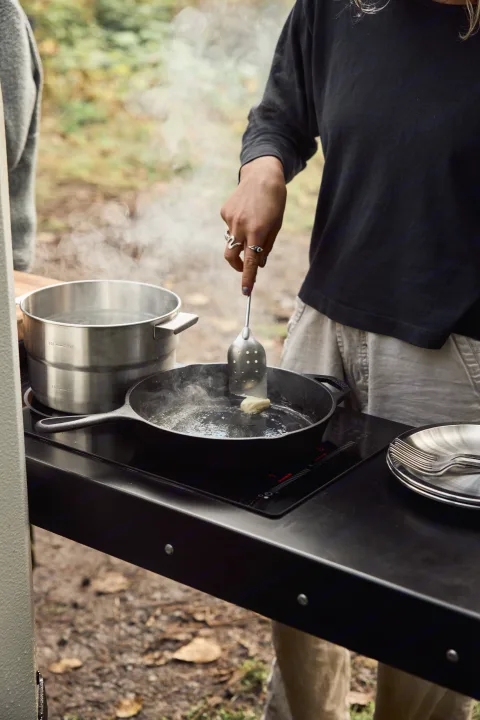 RV rental kitchen: Outdoor cooking on an induction stove. Steam rises from a pot, food fries in a cast iron pan.. Campworks NS-1 Electrified 2024