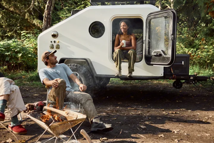 Relaxing with an RV rental: Woman in camper door, man by fire pit, dog rests on ground.. Campworks NS-1 Electrified 2024