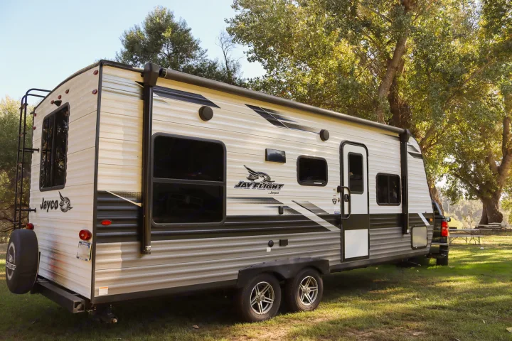 Enjoy this Jayco travel trailer RV rental, parked on lush grass in a scenic campground amidst bright trees.. Jayco Jay Flight SLX Rocky Mountain Edition 2022