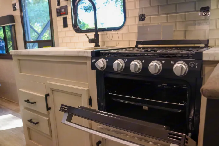 RV rental kitchen: modern gas range with open oven, sink, white counters, and subway tile backsplash.. Jayco Jay Flight SLX Rocky Mountain Edition 2022