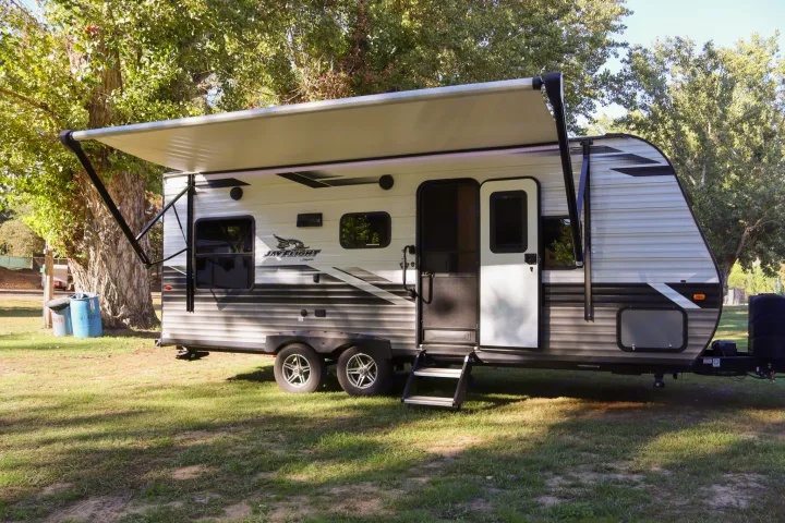 A modern Jay Flight travel trailer rv rental, white and gray with its awning extended, parked on a grassy campsite.. Jayco Jay Flight SLX Rocky Mountain Edition 2022