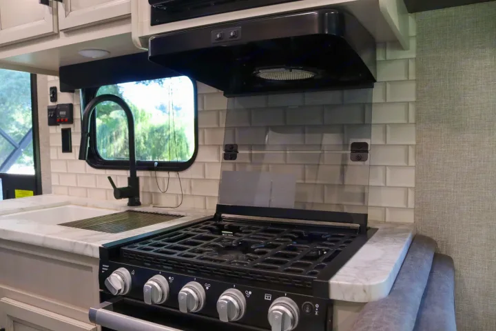 Modern RV rental kitchen with stove, sink, and stylish subway tile backsplash. Perfect for compact living on the road.. Jayco Jay Flight SLX Rocky Mountain Edition 2022