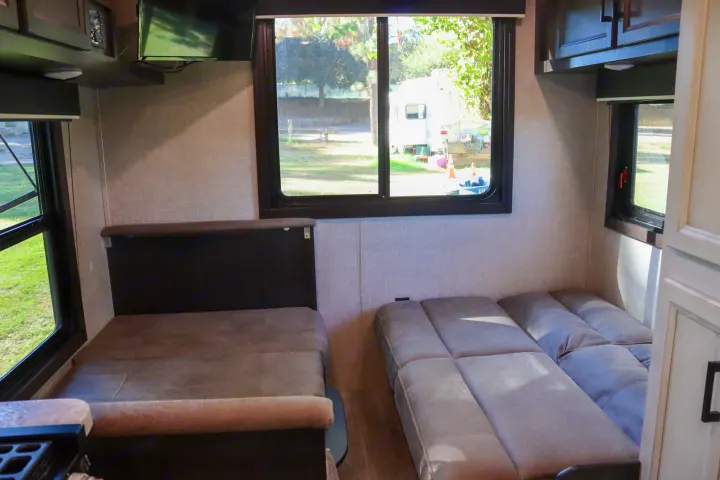 Cozy RV rental interior with a versatile dinette, convertible sofa, and large windows offering scenic views of the campground.. Jayco Jay Flight SLX Rocky Mountain Edition 2022