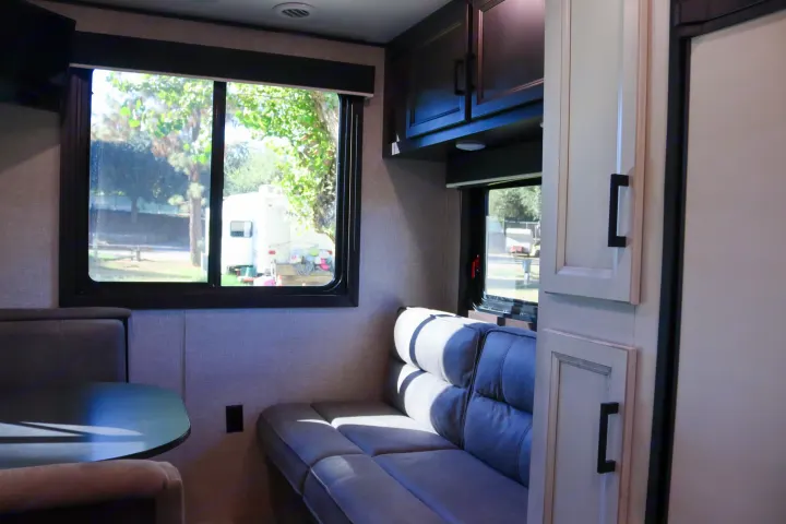Inside an RV rental: a cozy living area with a dining table, sofa, and outdoor views through large windows.. Jayco Jay Flight SLX Rocky Mountain Edition 2022
