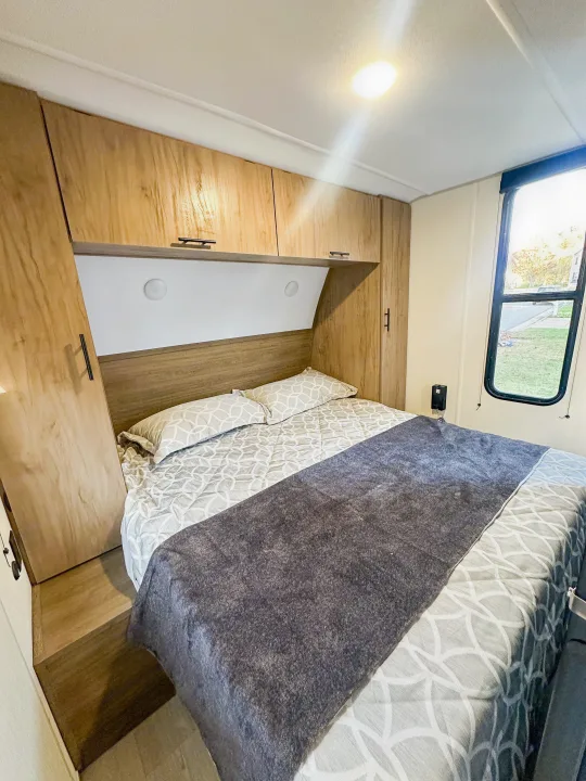 Experience comfort in this RV rental bedroom: light wood cabinetry, a snug bed with geometric bedding, and a large window.. Forest River Grey Wolf 26 DBH 2025