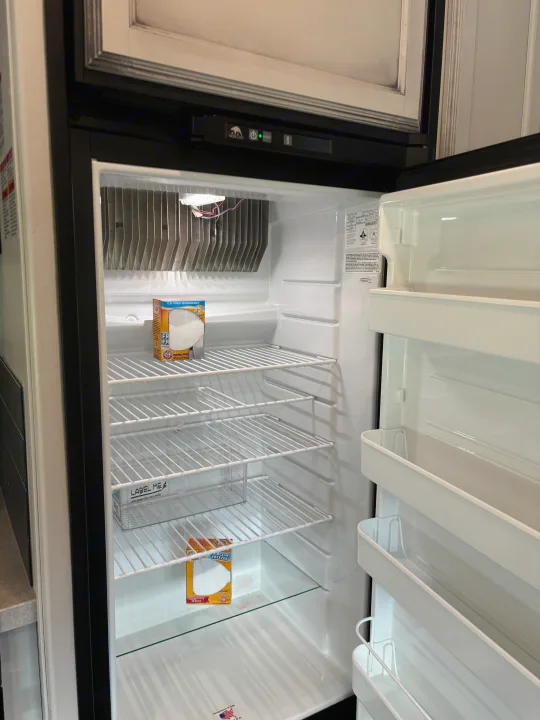 Inside an empty Norcold RV rental refrigerator, featuring wire shelves, door storage, and baking soda for freshness.. Jayco Greyhawk 2022