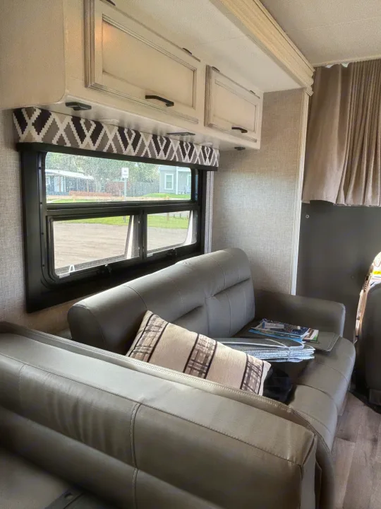 Cozy RV rental interior with comfortable sofa seating, overhead cabinets, and a window view.. Jayco Greyhawk 2022