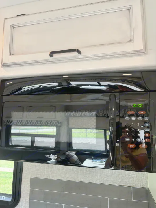 Inside this RV rental, find a black High Pointe microwave oven with a digital clock and various cooking options below white cabinets.. Jayco Greyhawk 2022
