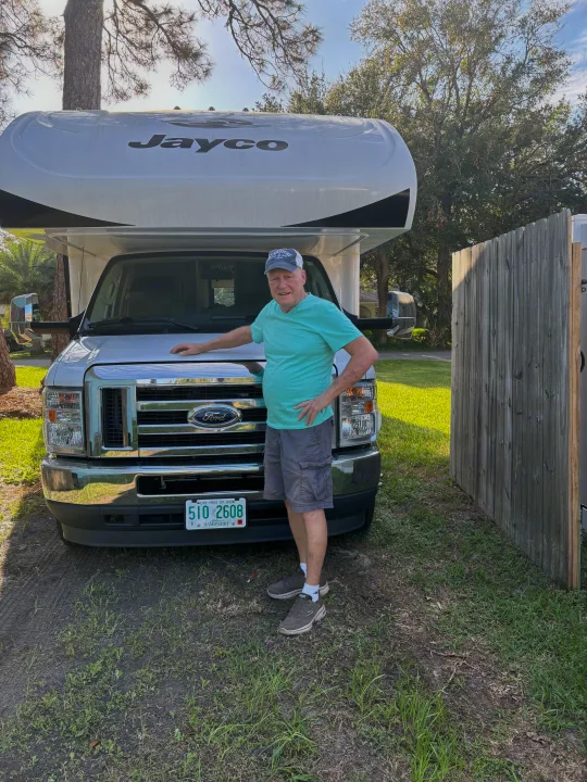 Older man smiles proudly beside his white Jayco RV rental, ready for travel adventures. New Hampshire plate visible.. Jayco Greyhawk 2022