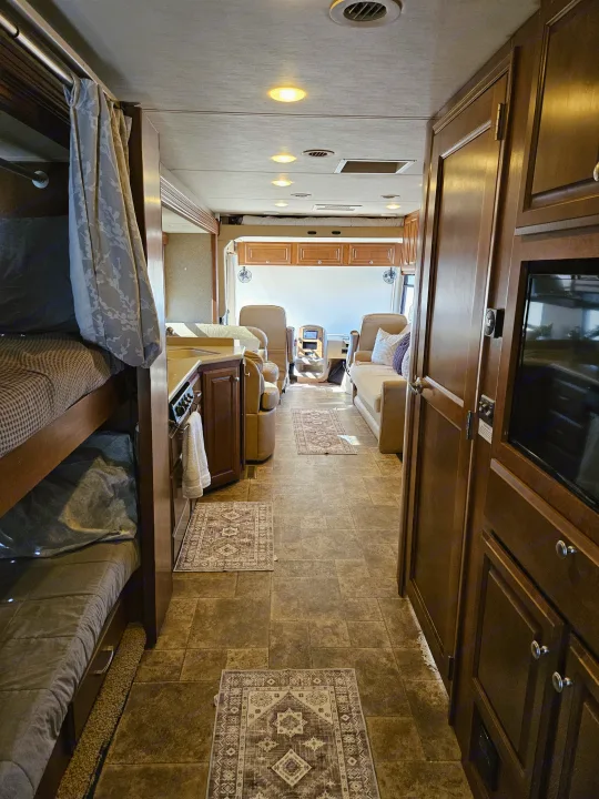 Inside a modern RV rental, showing bunk beds, kitchen, and forward cockpit area with tiled floor and warm lighting.. Thor Palazzo 2013