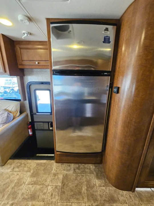 Inside this RV rental: a prominent stainless steel refrigerator, wood cabinets, and the main entry.. Thor Palazzo 2013