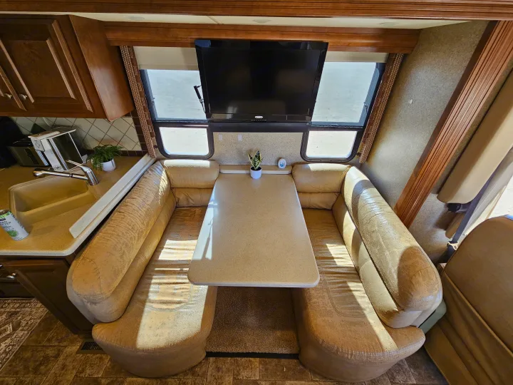 RV rental interior featuring a light-colored dinette booth, table, and overhead TV, with a kitchen sink to the left.. Thor Palazzo 2013
