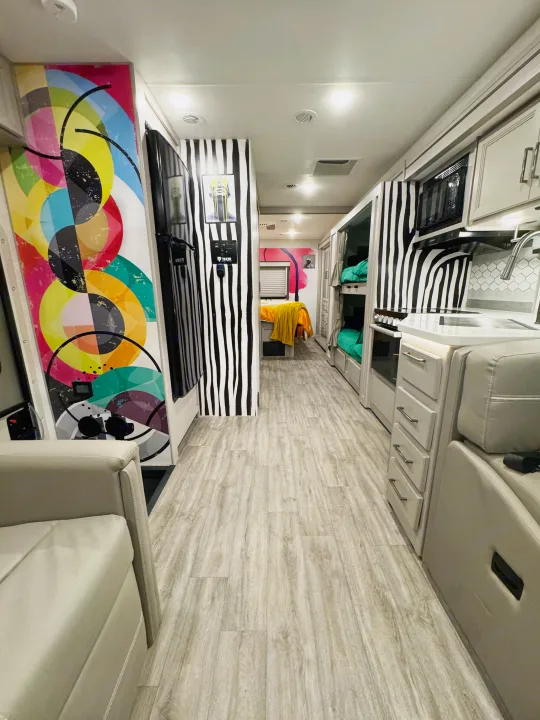This modern rv rental interior features a vibrant kitchen, bunk beds, and a colorful bedroom area with unique striped walls.. Thor Resonate 2024