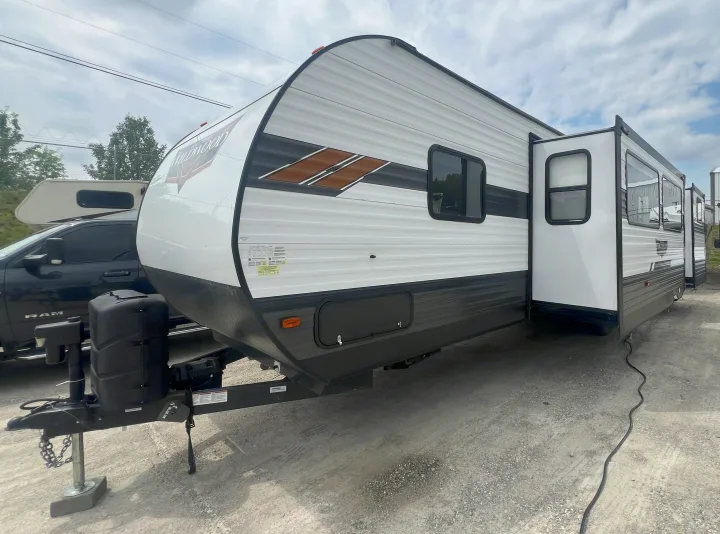 White Wildwood travel trailer RV rental with dark accents and extended slide-outs, parked on a gravel lot.. Forest River Wildwood 2021
