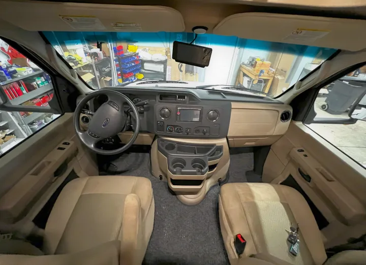 RV rental interior. Front cockpit view of a clean vehicle showing the dashboard, steering wheel, and two beige front seats.. Forest River Sunseeker 2016