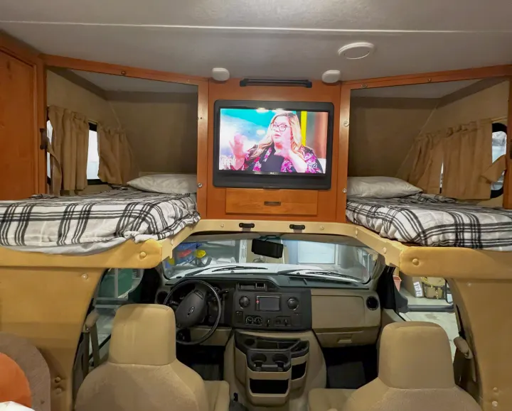 RV rental interior: cozy view with overhead bunk beds, plaid blankets, central TV, and the complete driver's cockpit.. Forest River Sunseeker 2016