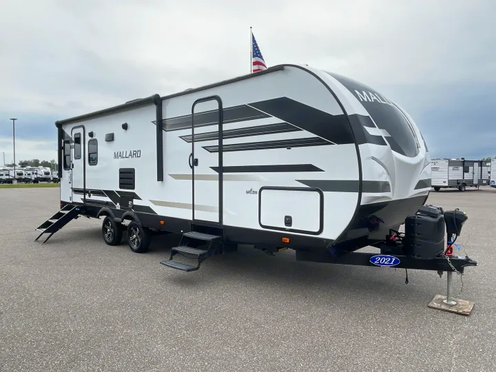 This white & black 2021 Mallard travel trailer with deployed steps, suitable for RV rental, flies a US flag.. Heartland RVs Mallard 2022
