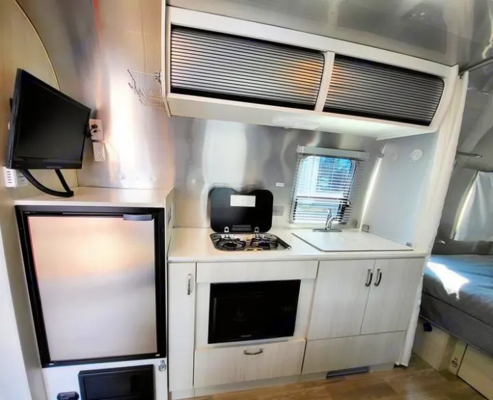Modern Airstream RV rental interior: A compact kitchen with fridge, stove, sink, microwave, and TV setup.. Airstream Bambi 2020