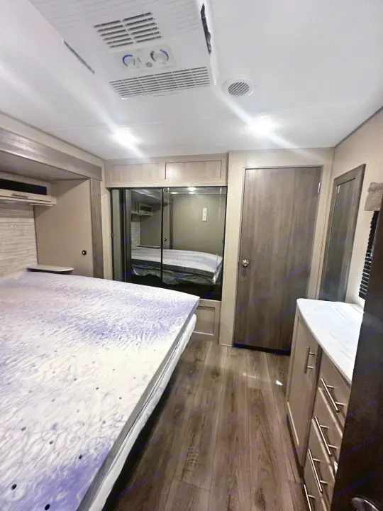 Comfortable RV rental bedroom featuring a large bed with unique topper, mirrored closet, and wood-look floor.. Coachmen 343bhts 2023