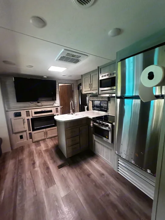 Modern RV rental interior featuring a full kitchen, living area with TV, electric fireplace, and wood floors.. Coachmen 343bhts 2023