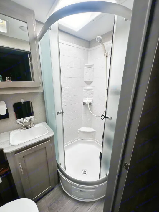 Detailed look at a modern RV rental bathroom featuring a curved shower, sink vanity, and mirror, designed for compact living.. Coachmen 343bhts 2023