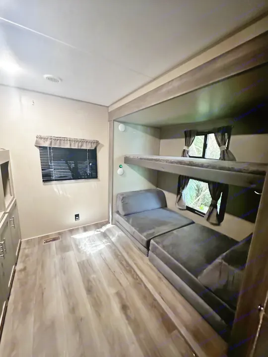Inside an RV rental: a comfortable bunk bed setup with a lower convertible lounge and bright window views.. Coachmen 343bhts 2023