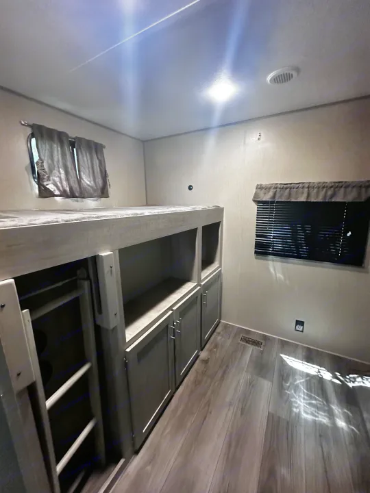 RV rental interior: bedroom with bunk beds, storage below, windows with blinds, wood floor, and ceiling vent.. Coachmen 343bhts 2023