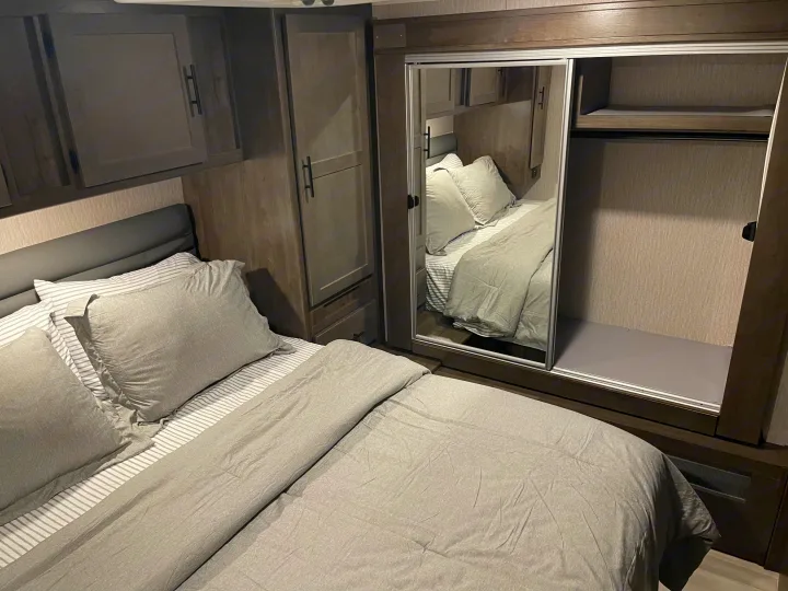 Spacious RV rental bedroom with a comfy bed, modern dark wood cabinetry, and mirrored sliding closet offering ample storage.. Forest River Coachmen Leprechaun Premier 2022