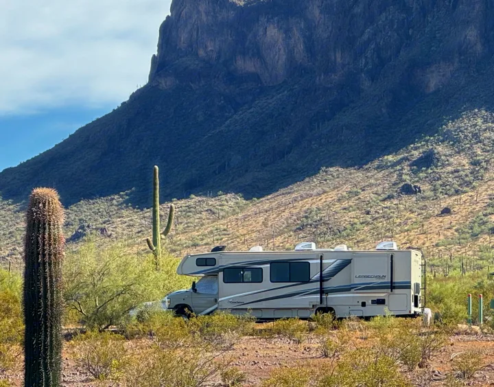 RV rental parked in a vast desert landscape with saguaro cacti and towering mountains in the background.. Forest River Coachmen Leprechaun Premier 2022