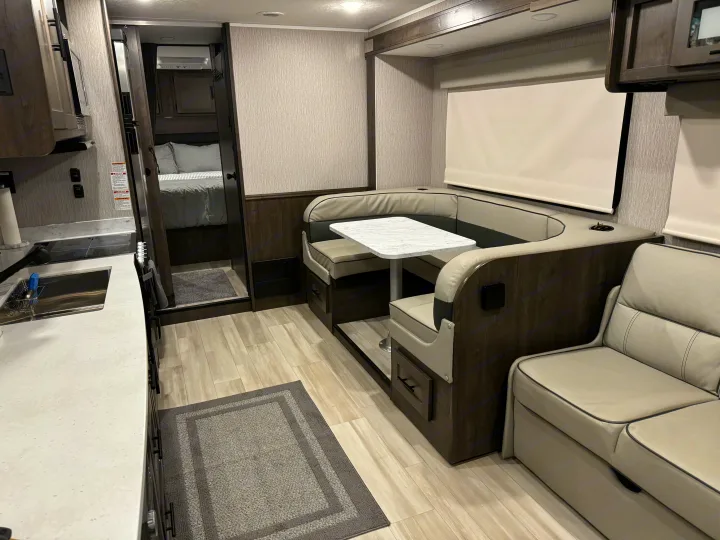 Modern RV rental interior with kitchen, U-shaped dinette, and visible bedroom.. Forest River Coachmen Leprechaun Premier 2022