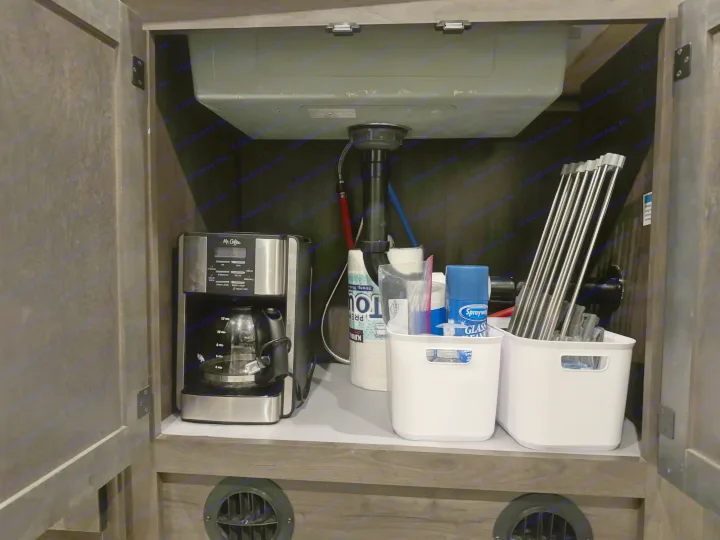 RV rental under-sink cabinet: Mr. Coffee, cleaning supplies, paper towels, and a roll-up drying rack are neatly stored.. Forest River Coachmen Leprechaun Premier 2022