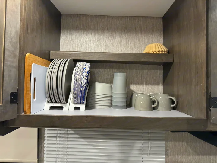 RV rental kitchen cabinet, neatly organized: plates, bowls, cups, and mugs stacked for space-saving, plus coffee filters above.. Forest River Coachmen Leprechaun Premier 2022