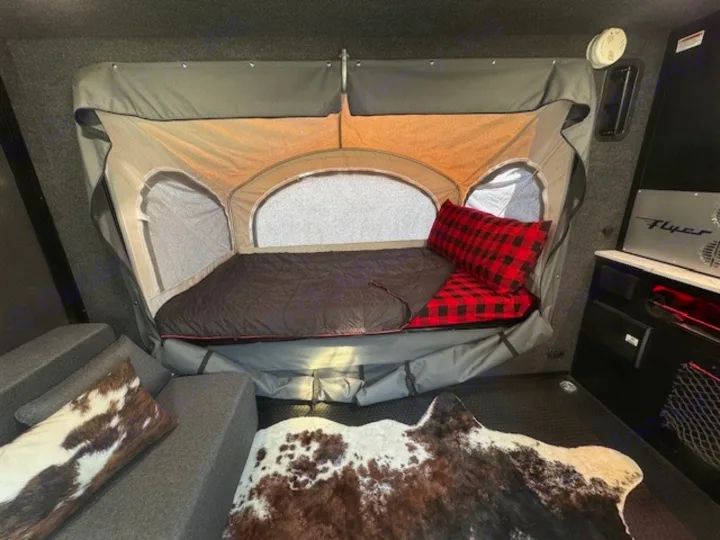 This RV rental interior shows a clever tent-style bed w/plaid pillow & sleeping bag, plus rustic cowhide decor.. InTech RV Flyer 2023