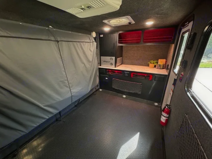 Spacious rv rental interior showing a large covered bed, a modern kitchen area with red shelves, and durable flooring.. InTech RV Flyer 2023