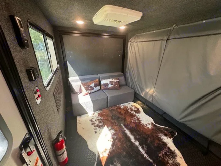 RV rental interior: cozy living space with modular grey sofa, cowhide rug, window, and ceiling AC unit. Fire extinguisher visible.. InTech RV Flyer 2023