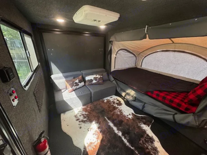 Modern RV rental interior with a fold-out bed, sofa, and rustic cowhide decor.. InTech RV Flyer 2023